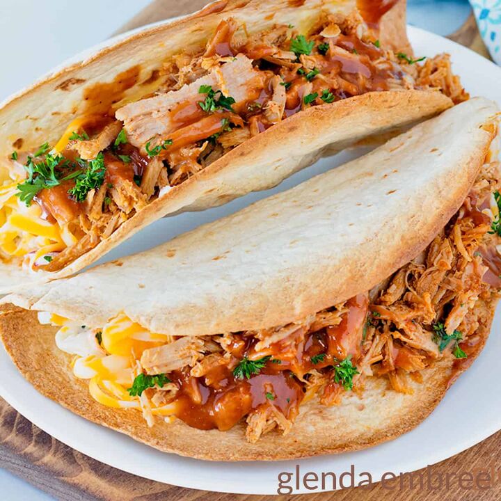 slow cooker pork carnitas, Two Pulled Pork tacos on a white plate with a blue and white print fabric napkin in the background