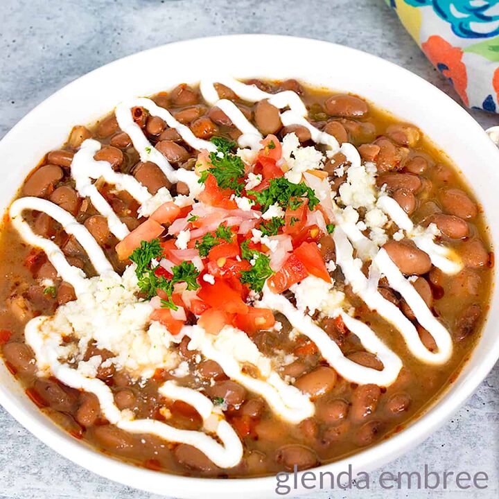 slow cooker pork carnitas, Slow Cooker Charro Beans in a white ceramic bowl and garnished with sour cream diced tomatoes green onion parsley and queso fresco