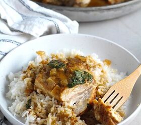 brazilian chicken in peanut sauce galinha com molho de amendoim, Fork holding a bit of a piece of Brazilian Chicken in Peanut Sauce on top of rice on a plate on counter with dish towel next to it Skillet with chicken in background