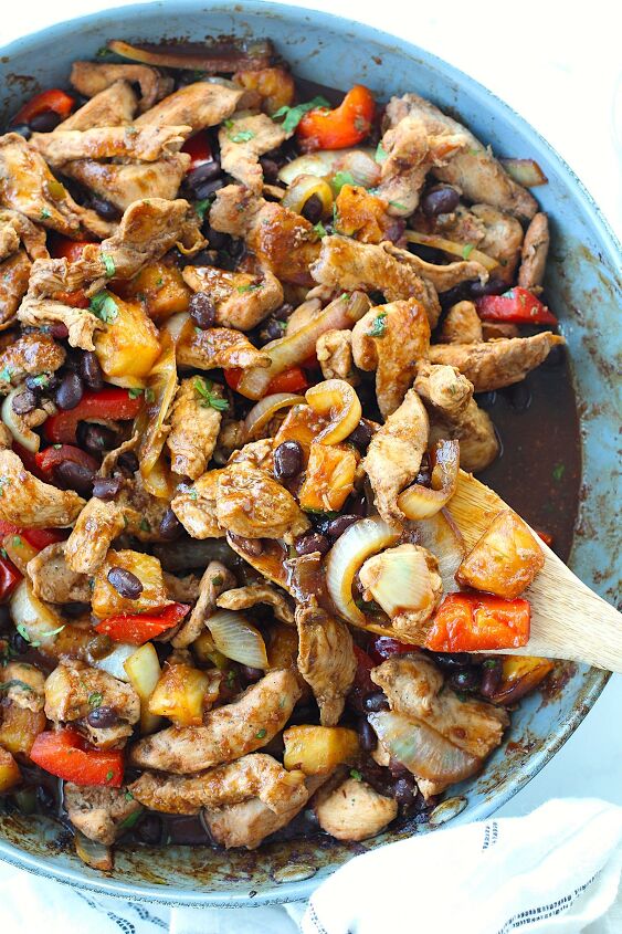 marinated chicken stir fry with pineapple and beans, Brazilian Marinated Chicken Stir Fry with pineapple black beans red Pepper and onions in a skillet with spatula with cilantro garnish It is truly one amazing dish with incredible flavor
