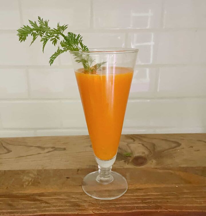 carrot mimosa, Single glass of carrot mimosa on a wood table with a white tile background