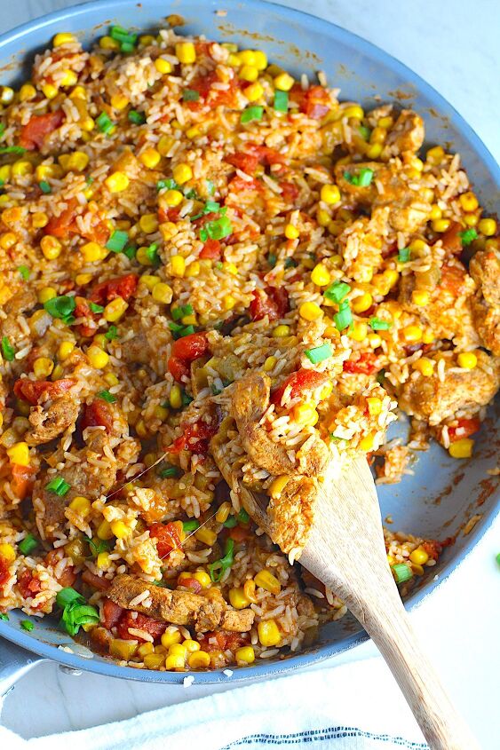 mexican marinated chicken and rice skillet, Mexican Marinated Chicken and Rice Skillet with tomatoes corn and scallions Spatula scooping inside the skillet