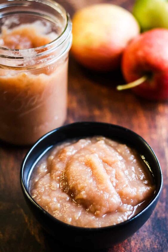 easy instant pot applesauce recipe, low angle vertical shot of homemade instant pot applesauce in a black bowl with a jar of applesauce and some apples in the background