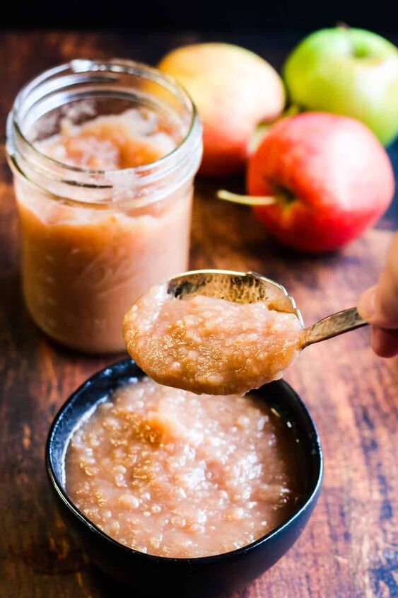 easy instant pot applesauce recipe, low angle vertical shot of homemade instant pot applesauce in a black bowl with a spoonful being lifted a jar of applesauce and some apples in the background