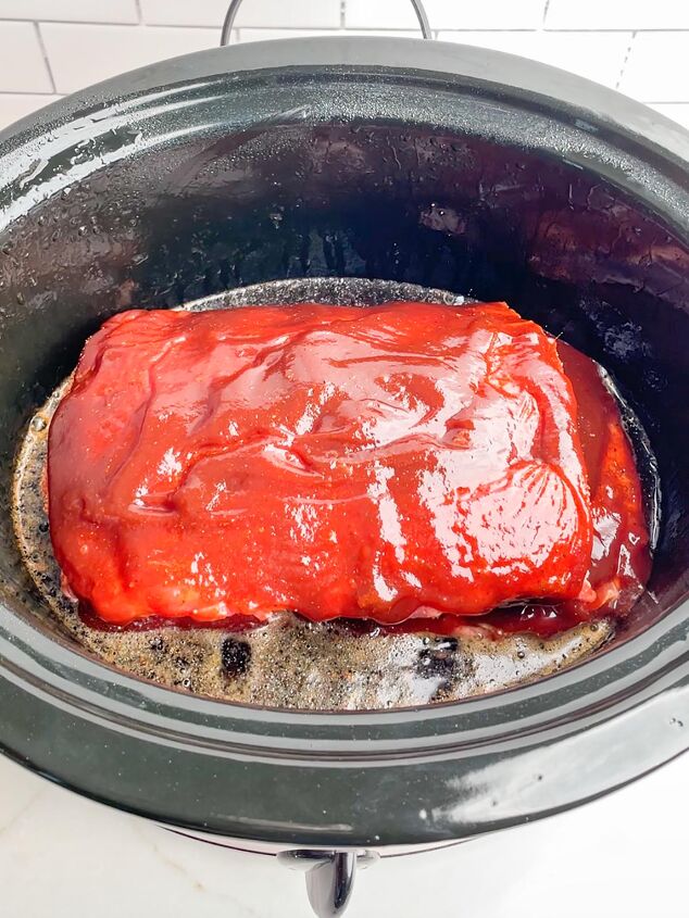 dr pepper crock pot ribs, ribs with BBQ sauce in a black slow cooker with Dr Pepper in the bottom