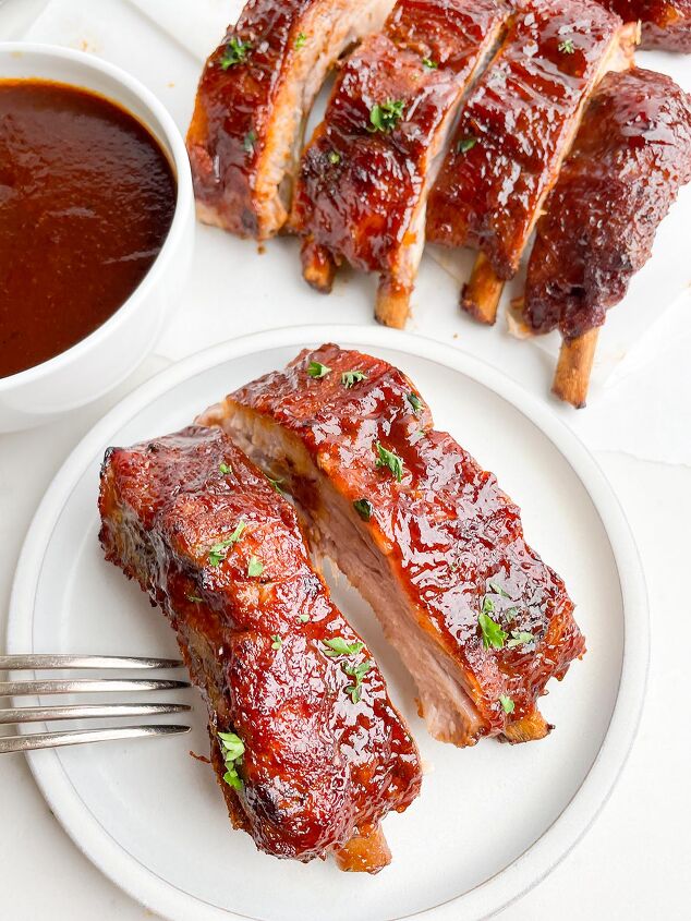dr pepper crock pot ribs, white plate with two ribs with bowl of BBQ sauce and more ribs in the background