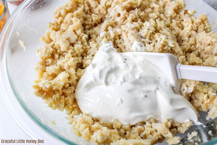 easy and delicious loaded baked potato casserole, Potato mixture in clear glass mixing bowl with sour cream sitting on top before being mixed together