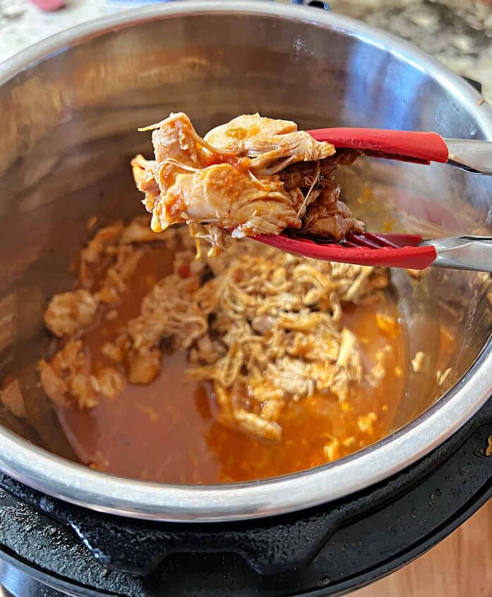instant pot salsa chicken only 3 ingredients, a tongs holding shredded salsa chicken over the instant pot full of more meat