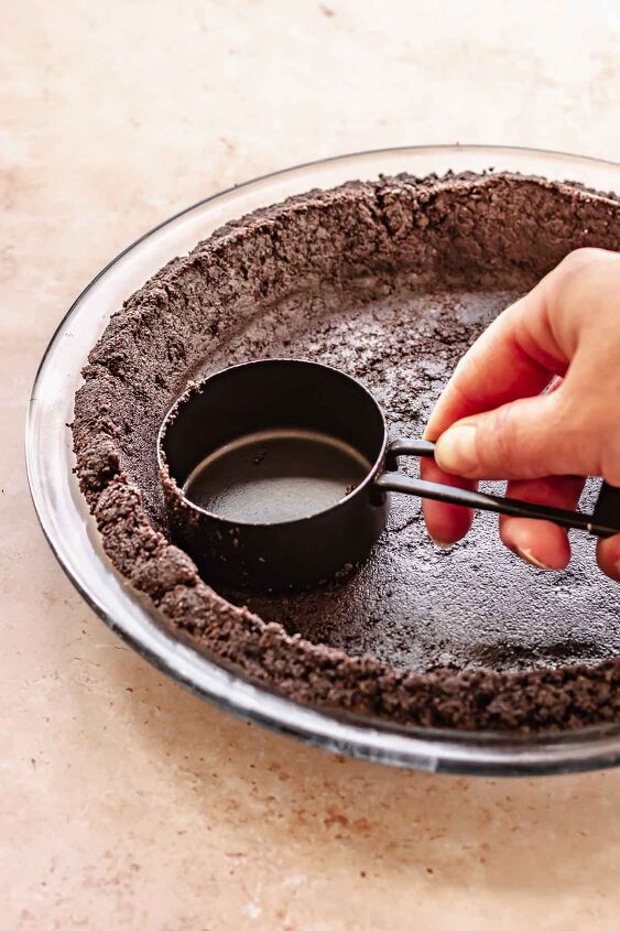 oreo peanut butter pie, A hand uses a measuring cup to press oreo crust into a pie dish