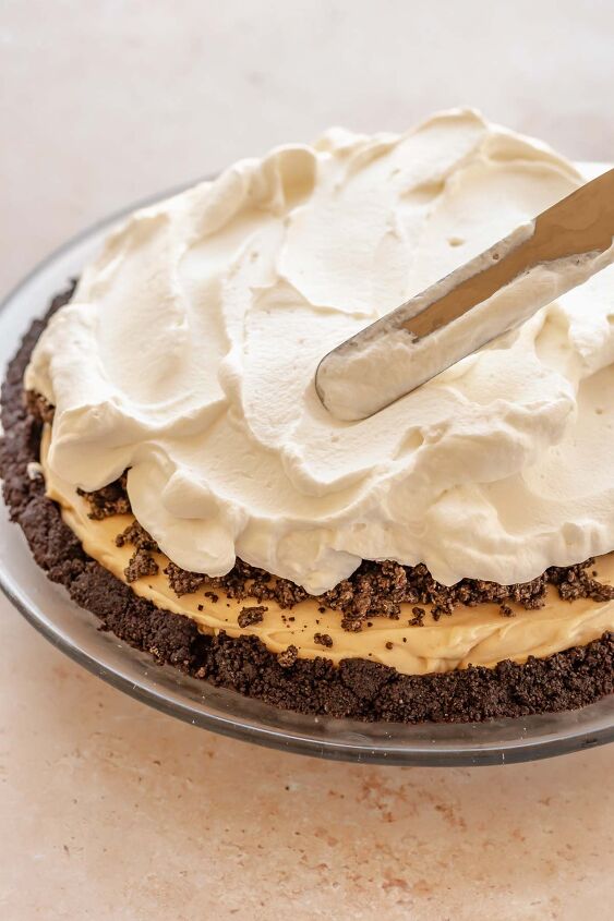 oreo peanut butter pie, An offset spatula spreads whipped cream on top of the pie