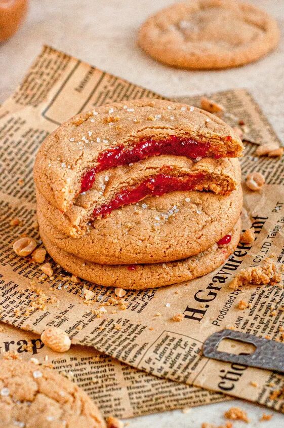 peanut butter and jelly cookies gluten free dairy free, A stack of 4 golden brown peanut butter cookies sitting on a brown piece of newspaper and surrounded by chopped peanuts