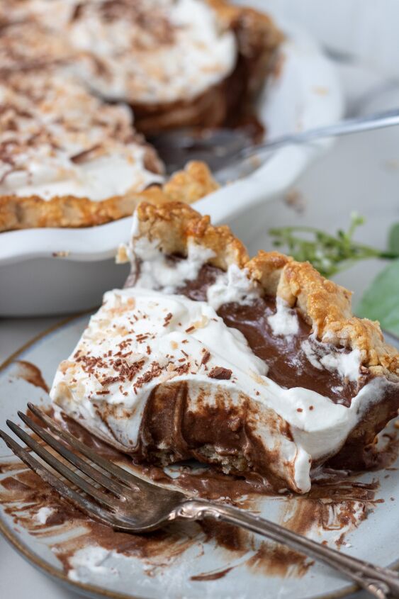 homemade chocolate coconut cream pie, A piece of coconut cream chocolate pie that s been eaten There s chocolate filling smeared on the plate with a fork There s a white pie plate in the background with the rest of the pie in it and a green flower in the background