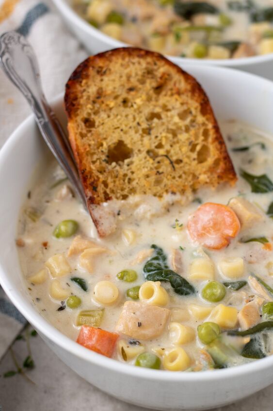 instant pot creamy chicken soup, A white soup bowl filled with creamy chicken soup There s a piece of garlic bread dipped in the bowl with a silver spoon