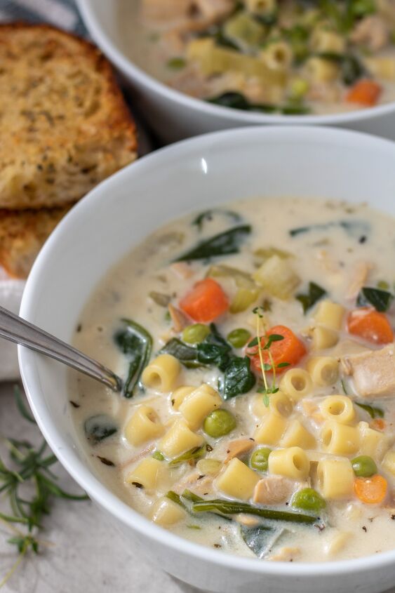 instant pot creamy chicken soup, A white bowl with chicken soup with pasta spinach peas and carrots The soup is creamy There s two pieces of golden crusty garlic bread next to the bowl