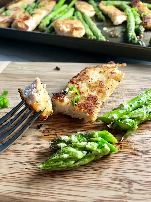 Parmesan breadcrumb chicken on cutting board with bite on fork and asparagus cut