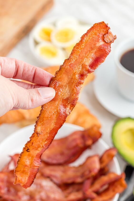 how to cook bacon in the air fryer, hand holding a slice of bacon cooked in the air fryer