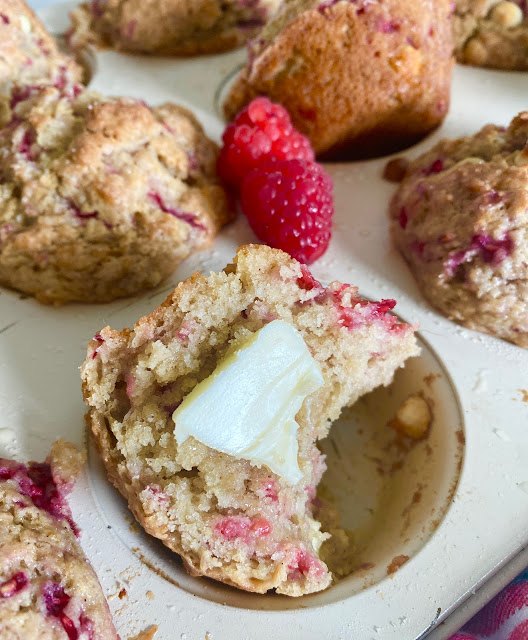white chocolate raspberry bakery muffins, Split white chocolate raspberry muffin with butter sitting in a muffin tin