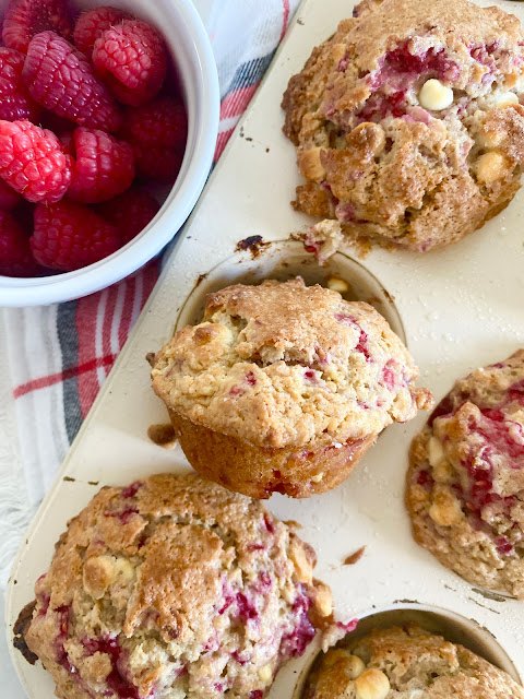 white chocolate raspberry bakery muffins, White ramekin holding raspberries next to a muffin tin full of raspberry muffins