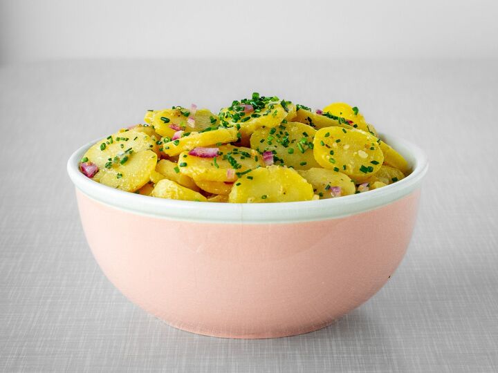 austrian potato salad, A pastel pink vintage bowl filled with potato salad placed on a grey vintage table