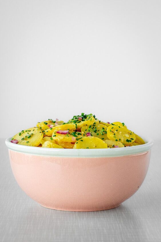 austrian potato salad, A pastel pink vintage bowl filled with potato salad placed on a grey vintage table