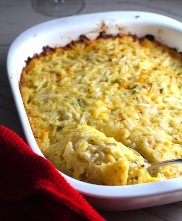 cheesy hash brown casserole without soup, Spoon scooping Cheesy Hash Brown Casserole in casserole dish on counter with red towel This recipe does not disappoint It s warm creamy and full of flavor And it s the perfect side dish for your holiday dinner