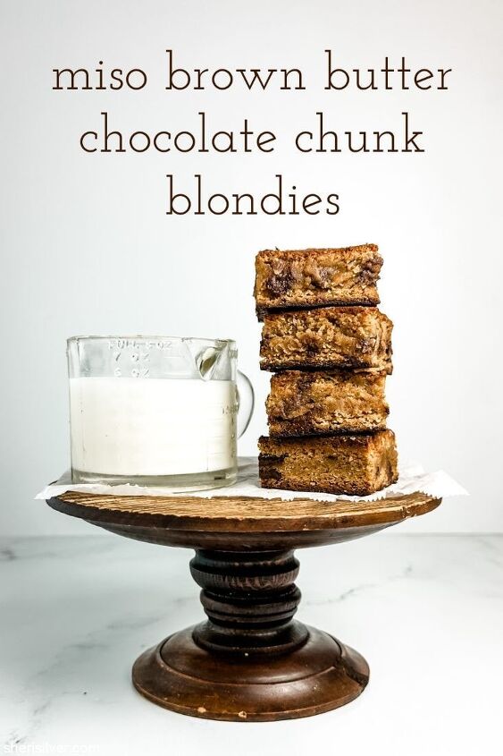 the best miso brown butter chocolate chunk blondies, miso brown butter chocolate chunk blondies on a wooden cake stand next to a vintage glass pitcher filled with milk