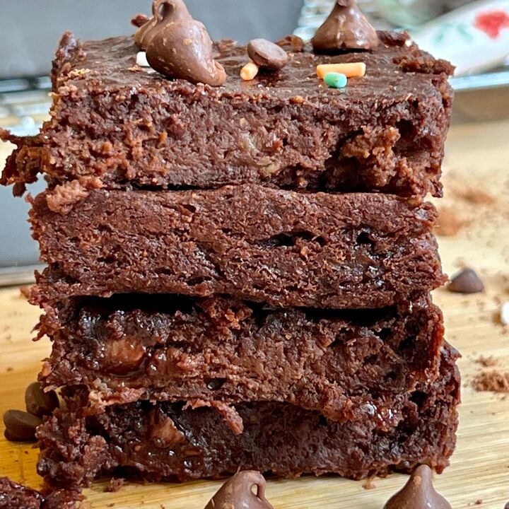 easy 3 ingredient brownies with bananas, a stack of four 3 ingredients brownies on a wooden cutting board with chocolate chips and colored sprinkles