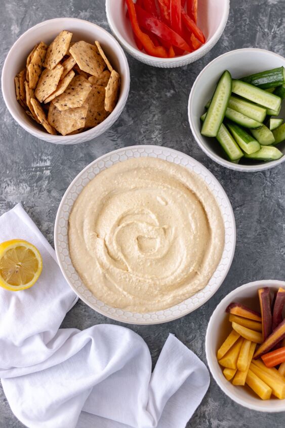 the best classic homemade hummus, A bowl of homemade hummus surrounded by smaller bowls of crackers bell pepper slices cucumber slices and carrot slices