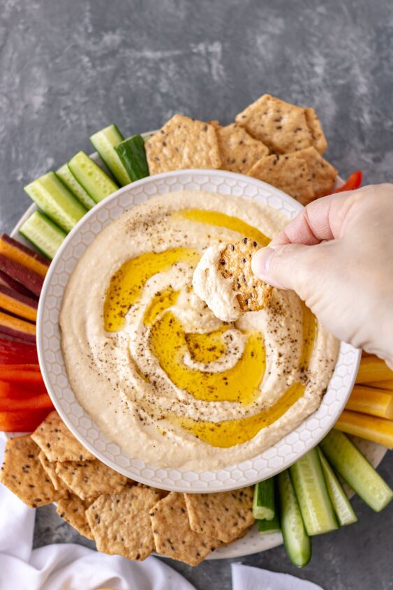 the best classic homemade hummus, A hand taking a swipe of hummus with a cracker
