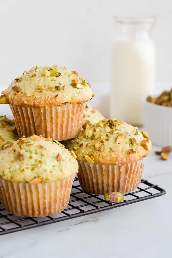 pistachio pudding muffins, Pistachio muffins stacked on wire rack with a glass of milk and a bowl of pistachios in background