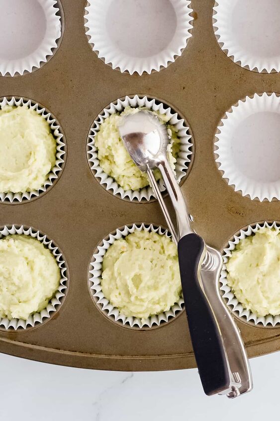 pistachio pudding muffins, Metal and black cookie scoop resting in a filled muffin tin with batter