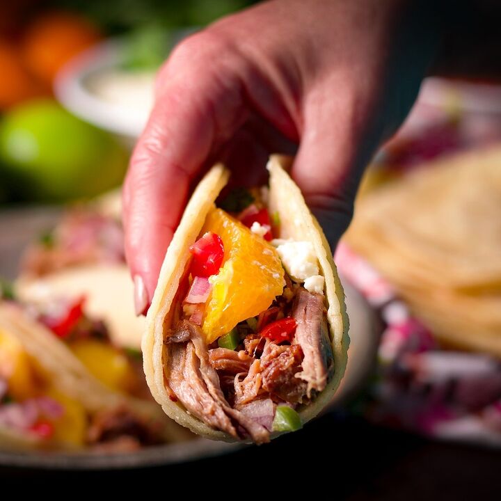 camping tacos shredded pork with pico de gallo, Someone using their hand to lift a shredded pork taco with oranges pico de gallo and queso fresco from a plate of tacos