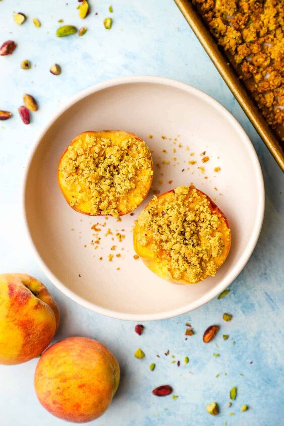 roasted peaches with pistachio crumble, A bowl with two roasted peach halves topped with pistachio crumble