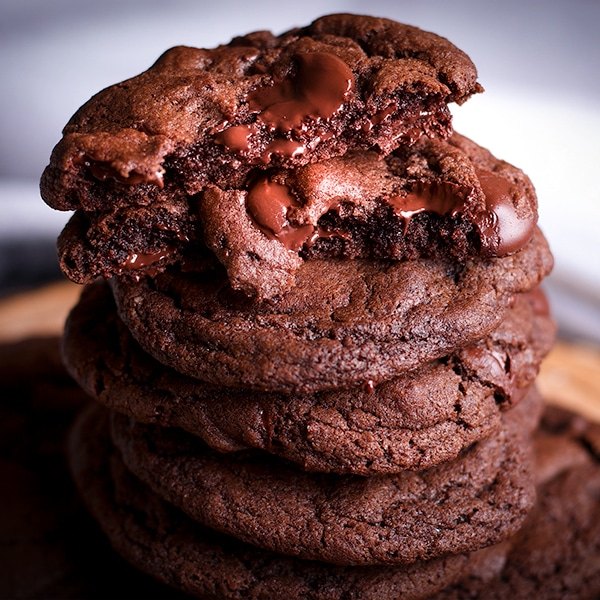 A stack of double chocolate Anything Cookies with the top cookie broken open so you can see the gooey chocolate middle