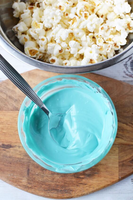 Melted blue candy melts in a bowl next to popcorn