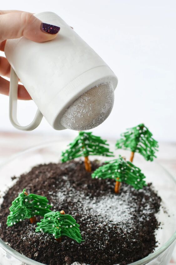 chocolate winter trifle with edible evergreen trees, Sprinkling powdered sugar on top of a winter wonderland trifle