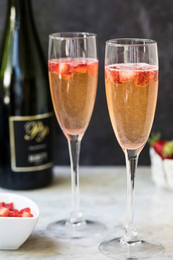 strawberry mimosa, two flutes of strawberry mimosas with strawberries and champagne bottle in background