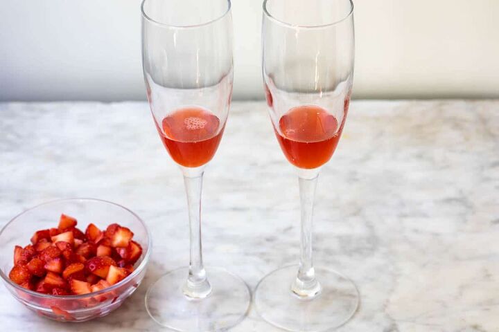 strawberry mimosa, two glasses of champagne filled with a small amount of strawberry syrup and bowl of strawberries