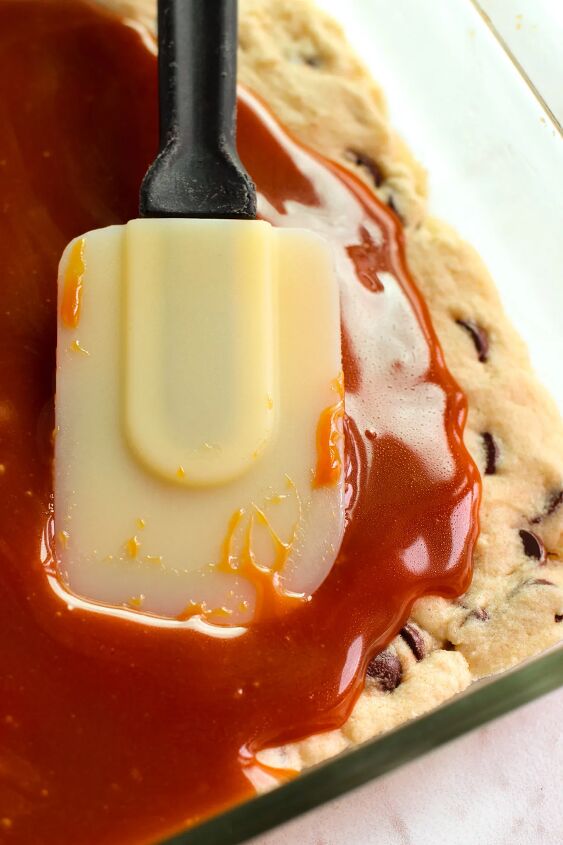 salted caramel chocolate chip cookie bars recipe, Using a spatula to smooth caramel over a cookie