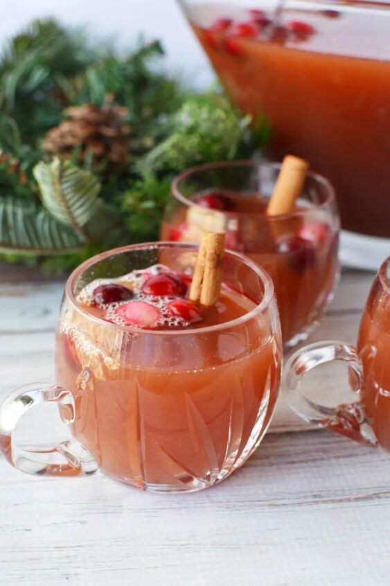 cranberry and cinnamon christmas punch recipe, Clear glass of punch with cranberries and cinnamon sticks with holiday decor on the table