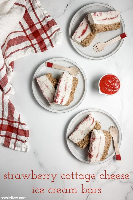 high protein strawberry cottage cheese ice cream bars, strawberry cottage cheese ice cream bars on white plates with a bowl of strawberry puree and a red and white linen napkin