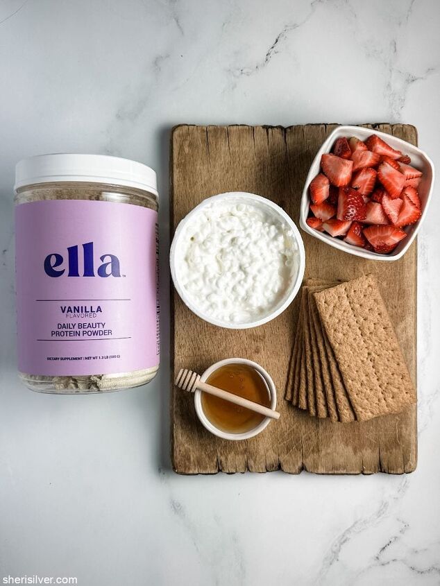 high protein strawberry cottage cheese ice cream bars, cottage cheese in a bowl with a bowl of strawberries a stack of graham crackers and a bowl of honey on a wooden board next to a jar of Ella protein powder