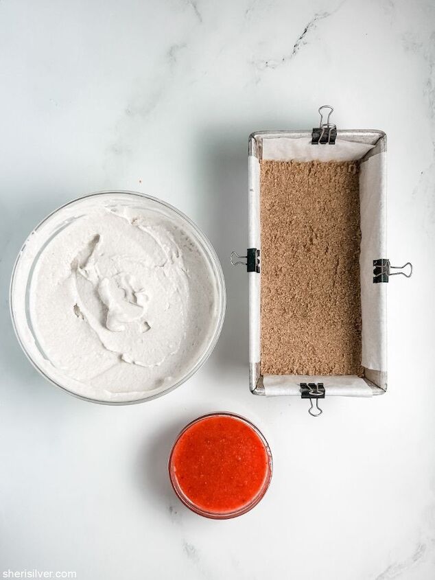 high protein strawberry cottage cheese ice cream bars, loaf pan with graham cracker crust next to bowls of cottage cheese ice cream and strawberry puree