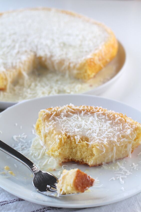 brazilian coconut cake bolo de coco, Brazilian Coconut Cake piece on a plate with a bite taken out and the rest of the cake on a platter in the background
