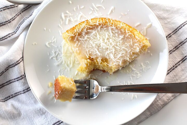 brazilian coconut cake bolo de coco, Brazilian Coconut Cake piece on a plate with a bite taken out and the rest of the cake on a platter in the background