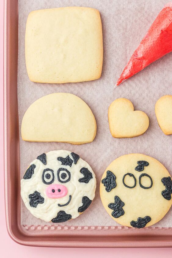 udderly sweet cow valentine sugar cookies, Cut out cookies on a baking sheet with icing and one decorated cow cookie and one in the process