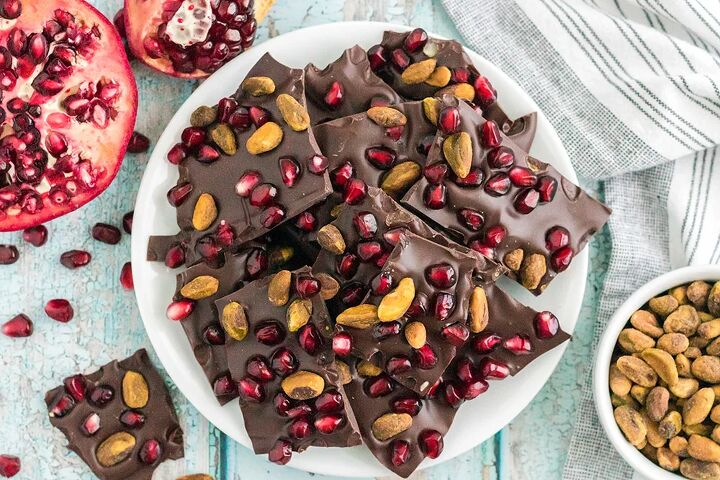 chocolate pomegranate bark with pistachios, Chocolate bark candy with pomegranates and pistachios on a plate next to nuts and pomegranates on the table