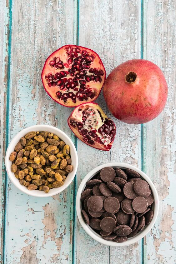 chocolate pomegranate bark with pistachios, A sliced pomegranate bowl of pistachios and bowl of dark chocolate wafers on a table