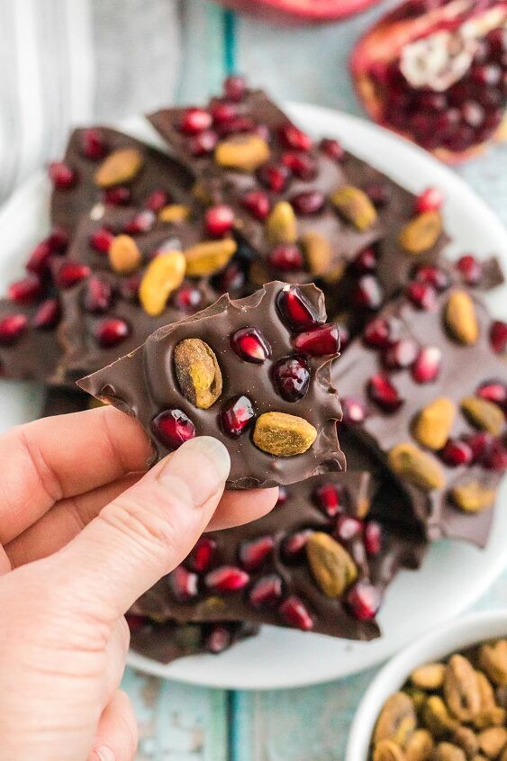 chocolate pomegranate bark with pistachios, Holding a piece of chocolate pomegranate with pistachios candy over the plate full of the pieces