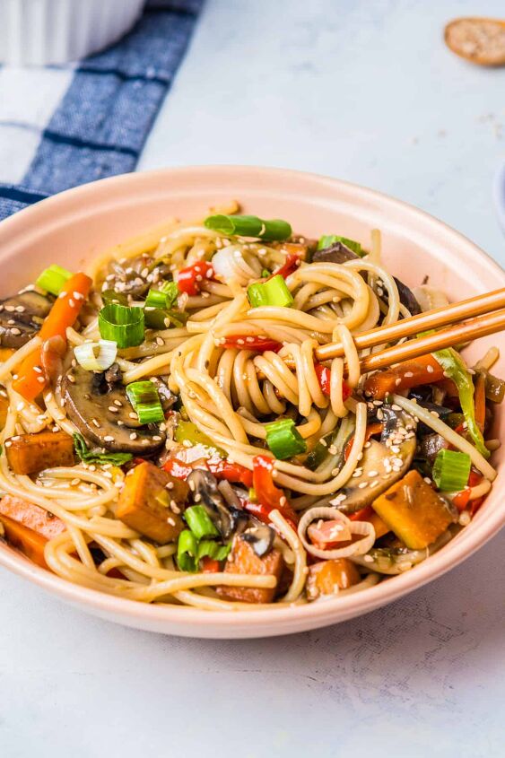 vegan stir fry noodles ready in under 30 minutes, Stir fry noodles with tofu eggplant and bell pepper in a pink bowl with chopsticks